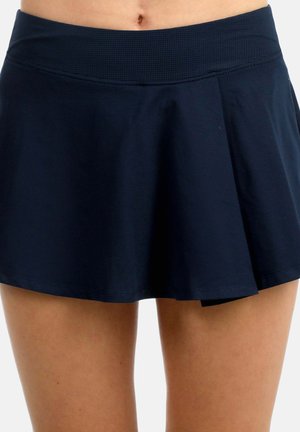 Falda deportiva azul marino con pliegues, llevada en la cintura, mostrando el abdomen y la parte superior de las piernas.