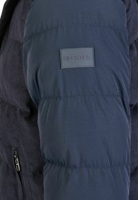 Navy pufferjack met een mix van glad nylon en textiel; beschikt over een zichtbare HECHTER-label op de schouder en een ritszak.