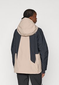Vodoodporna jakna z bež in mornarsko modrim barvnim blokom, nastavljiva kapuca ter sproščen fit z stranskimi žepi.