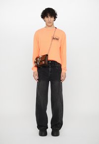 Neon orange langærmet skjorte med sort logo, parret med sorte baggy jeans med side-syning. Accessory: brun crossbody taske.