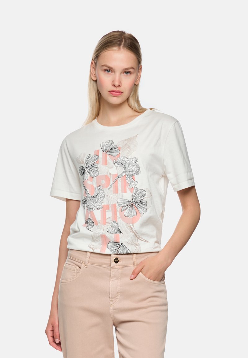 White cotton t-shirt featuring floral graphics in black and peach tones, paired with light beige pants. Short sleeves and relaxed fit.