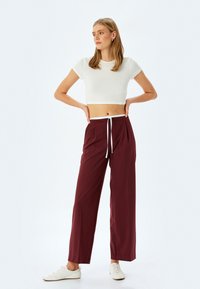 Pantalons larges bordeaux avec taille à cordon blanc et plis sur le devant. Associés à un crop top blanc ajusté et des baskets blanches. Texture de tissu lisse.