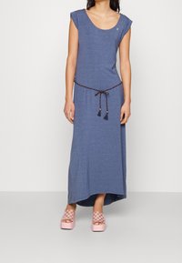 Niebieska maxi sukienka bez rękawów z okrągłym dekoltem, plecionym paskiem w talii i frędzlami. Do tego różowe sandały na platformie w kratę.