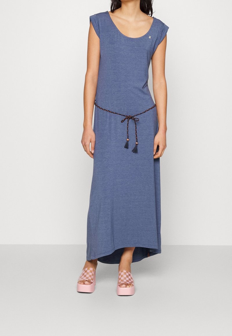 Niebieska maxi sukienka bez rękawów z okrągłym dekoltem, plecionym paskiem w talii i frędzlami. Do tego różowe sandały na platformie w kratę.