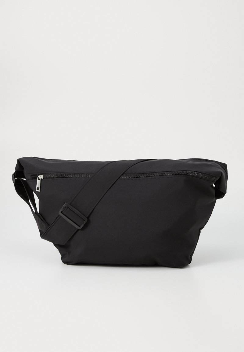 Bolsa de ombro de tecido preto com um design elegante, fecho superior com zíper, alça ajustável e uma textura suave. Compacta e funcional.