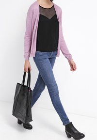 Light pink cardigan, black mesh-top, blue skinny jeans, black tote bag, and ankle boots; smooth texture and casual design.