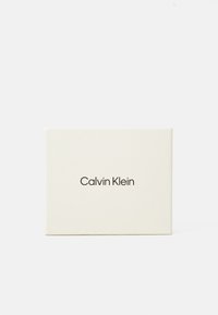 Emballage Calvin Klein dans une douce teinte crème, avec une forme rectangulaire simple et un logo noir minimaliste à l'avant.