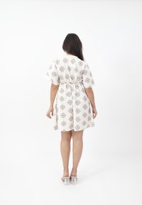 Abito bianco corto con vita stretta, caratterizzato da motivi geometrici grigi. La modella indossa sandali con tacco a blocco trasparente.