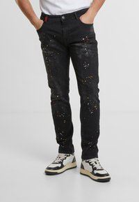 Czarne dżinsy z denimu z kolorowymi plamami farby, w dopasowanym kroju, pięć kieszeni, a także czerwoną wszywką w pasie.