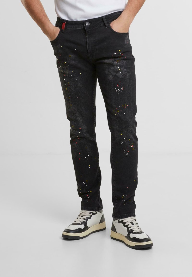 Czarne dżinsy z denimu z kolorowymi plamami farby, w dopasowanym kroju, pięć kieszeni, a także czerwoną wszywką w pasie.