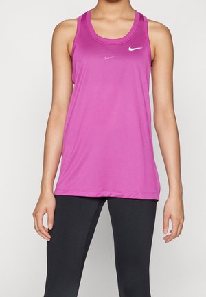 Frau trägt ein ärmelloses lila Nike Sporttanktop und schwarze Leggings, steht vor einem schlichten hellen Hintergrund.