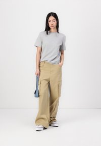 Grijze katoenen T-shirt gekoppeld aan losse kaki cargo broek met zijzakken. Het model houdt een lichtblauwe handtas vast en draagt witte sneakers.