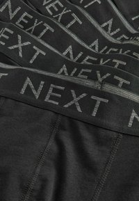 Black men's underwear with grey elastic waistbands branded with the word "NEXT" stacked in a layered arrangement.