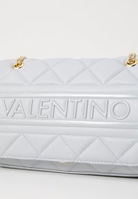 Pletena siva usnjena torbica z izstopajočim embosiranim logotipom "Valentino" in zlatimi verižnimi akcenti.