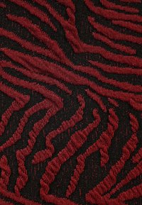 Textil mit schwarzem Grund und erhabenen, wellenförmigen roten Streifen. Die Oberfläche wirkt strukturiert und betont die Räumlichkeit des Musters.