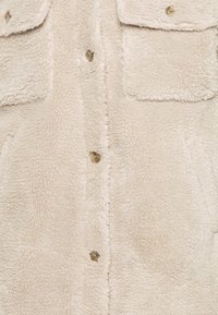 Krémově zbarvená mikina-košile z fleecu s dvěma náprsními kapsami, rychlosklaopkami a měkkým, texturovaným povrchem.