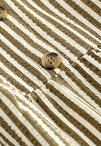 Gros plan d'un tissu rayé marron et blanc avec un motif texturé et deux boutons ronds beiges cousus dessus.