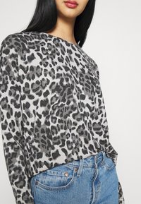 Graues und schwarzes Leopardenmuster Langarmshirt mit lässiger Passform, kombiniert mit hellblauen Jeans aus Denim mit kupfernen Nieten.