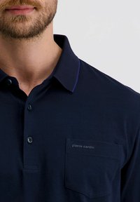 Marineblauw polo shirt met een knoopsluiting bij de kraag, een textuur stof, en een linkerknoopzak met "pierre cardin" branding.