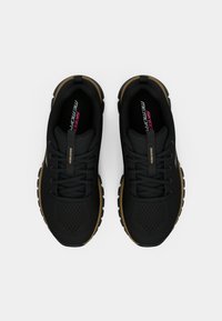 Schwarze Sportschuhe mit einem atmungsaktiven Mesh-Obermaterial, goldenen Akzenten an der Außensohle und strukturierten Schnürsenkeln. Mit "SKECHERS"-Logo.