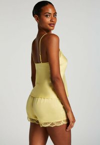 Geel satijnen slaapset met een camisole met kantaccenten en bijpassende shorts met kantopmerking, die een comfortabele pasvorm en een gladde textuur benadrukken.