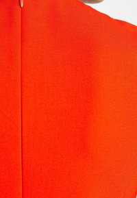 Jasně oranžová látka s hladkým povrchem, obsahující středový šev a jemný lesk. Minimalistický design bez dalších vzorů nebo akcentů.