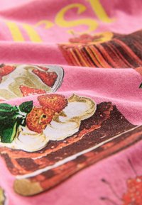 Pink fabric featuring printed dessert illustrations, including cakes and strawberries. Text in yellow is partially visible.