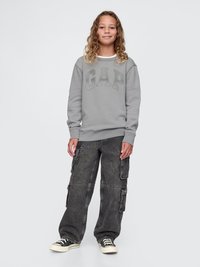Szara bluza z logo "GAP", w połączeniu z czarnymi spodniami cargo z licznymi kieszeniami. Model nosi czarno-białe sneakersy.