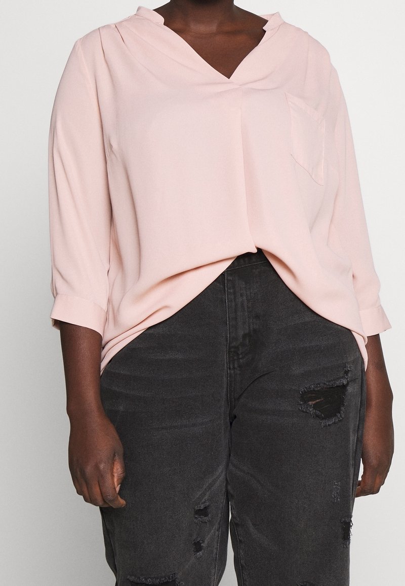 Blada różowa bluzka z dekoltem w serek i długimi rękawami, z przednią kieszenią. Połączona z czarnymi jeansami w stylu vintage, z dziurami i postrzępionymi brzegami.