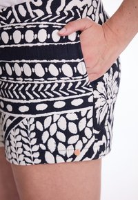 Marineblaue Shorts mit weißen Blatt- und Punktmustern, ausgestattet mit einer Seitentasche und einem kleinen Kupfer-Hauptknopf. Die strukturierte Stoffqualität verleiht Tiefe.