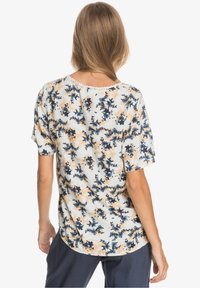 Blusa de manga corta en una tela ligera, con un estampado floral en azul marino, durazno y verde. Dobladillo redondeado y delicado encaje en el escote.