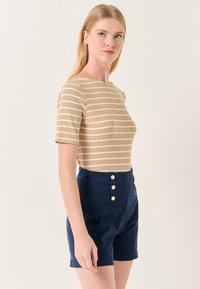 Gestreept beige top met een bootneck en korte mouwen, gecombineerd met marineblauwe high-waisted shorts met gouden knoopdetails.
