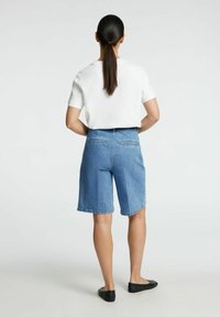 Denimshorts i ljusblått, hög midja och avslappnad passform, med två bakfickor och en ren fåll. Kombination med en vit topp med kort ärm.