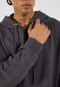 Szary hoodie z bawełny, z przednią kieszenią, kapturem ze sznurkiem i ściągaczami na mankietach. Haftowane logo na rękawie.