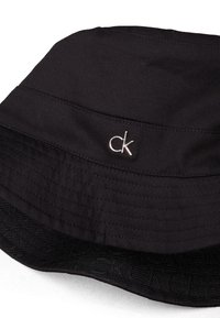 Czarny kapelusz typu bucket wykonany z gładkiego materiału, z obszytym paskiem i metalowym logo "ck" z przodu. Teksturowane czarne wnętrze.