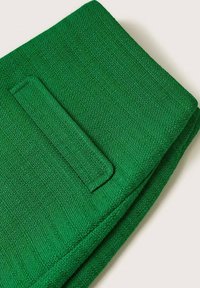 Tissu vert avec un tissage texturé. Comprend une poche patch rectangulaire et des bords pliés. Couleur vive et design structuré.