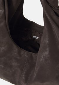 Sac fourre-tout en cuir marron avec une texture douce, grande ouverture et doublure en tissu. L'étiquette intérieure indique "WEEKDAY". Design léger.