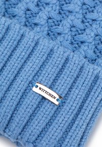 Modrá pletená čepice s texturovaným vzorem a žebrovaným lemem. Obsahuje stříbrnou štítek s nápisem "WITTCHEN" připevněný modrou nití.