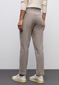 Ljus taupe byxor med avslappnad passform, som har en mjuk textur, bakfickor och uppvikta fållar, kombinerat med vita sneakers.