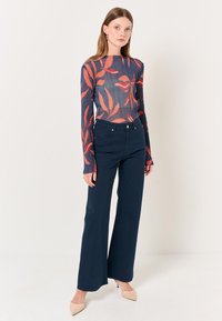 Maglietta a maniche lunghe con un motivo di foglie blu e arancioni; abbinata a pantaloni a gamba larga navy a vita alta; modella con tacchi a punta color nude.