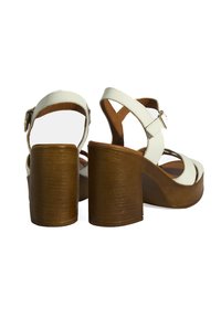 Sandales plateforme en cuir vegan blanc avec un talon en bois, bride de cheville ajustable et design ouvert à l'avant. Présente des brides croisées et une texture lisse.