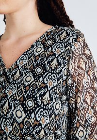 Μαύρο και μπεζ καπιτονάρισμα με περίπλοκα γεωμετρικά και ανθοφόρα σχέδια, που διαθέτει απαλή υφή και V λαιμόκοψη.