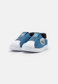 Blå slip-on sneakers med vit gummikapp, med en blå textilövre, svart foder och silvriga randiga detaljer.