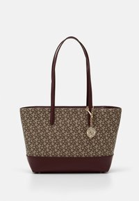 Sac fourre-tout monogramme marron avec de longues poignées en cuir marron foncé et un charme circulaire doré suspendu à une des poignées.