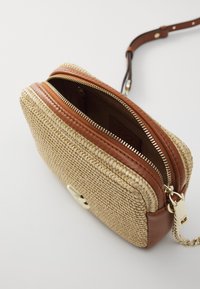 Tkaná taška z přírodních vláken s hnědými koženými akcenty, zlatým zipem a odnímatelným popruhem. Nabízí prostorný vnitřek.