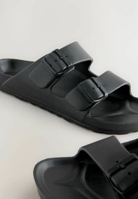 Sorte sandaler med to justerbare remme og spænder, lavet af tekstureret plastik, med en formet fodseng og en holdbar sål.