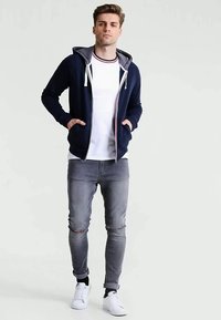 Námornícka mikina na zips s svetlosivým podšívkov, bielym tričkom, sivými zničenými džínsoch a bielymi teniskami. Kapucňa má šnúrky; pohodlný strih.