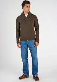 Brauner Rippenpullover mit Schalkragen, kombiniert mit hellblauen Jeans und braunen Schuhen. Der Pullover hat lange Ärmel und eine taillierte Passform.