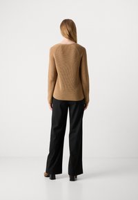 Pull à côtes marron avec un col rond, des manches longues et une silhouette ajustée, associé à un pantalon ample noir et des chaussures à talons marron.