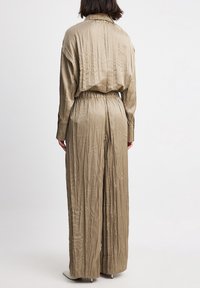 Beżowy, pomarszczony kombinezon z długimi rękawami, zebranym w talii oraz szerokimi nogawkami. Posiada kołnierz i delikatny połysk.